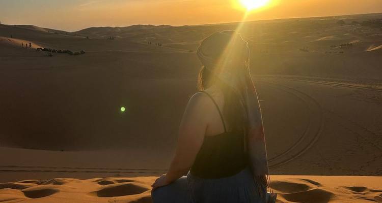 El viajero se sienta en una duna de arena mirando cómo el sol se pone sobre las olas infinitas del desierto del Sahara.