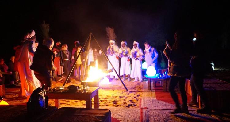 Personas bailando y tocando instrumentos alrededor de una fogata por la noche.