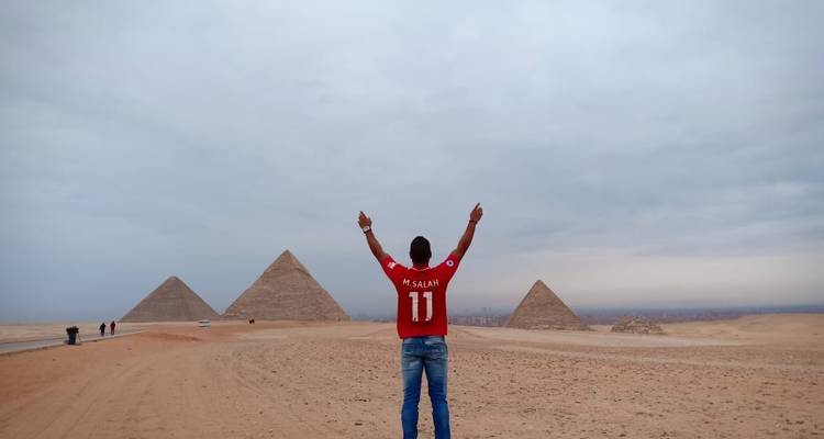 Persoon poseert met opgeheven armen voor de Piramides van Gizeh.
