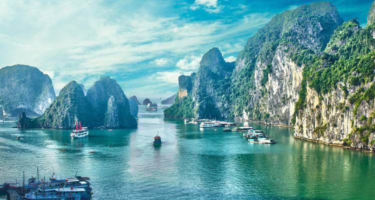 Halong Bay met kalkstenen karstformaties en boten onder een levendige hemel.