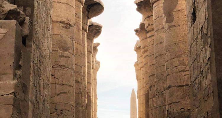 Columnas del antiguo Egipto con jeroglíficos, un obelisco visible en la distancia