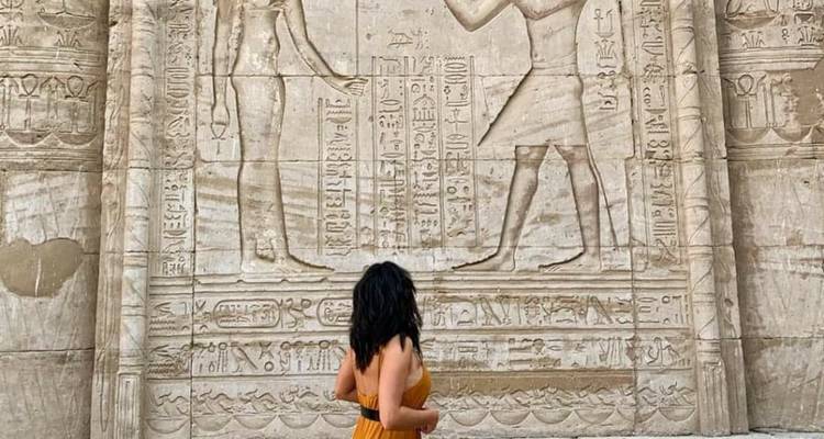 Mujer de pie frente a un relieve jeroglífico egipcio