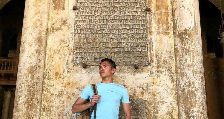 Hombre parado frente a una pared con inscripciones árabes