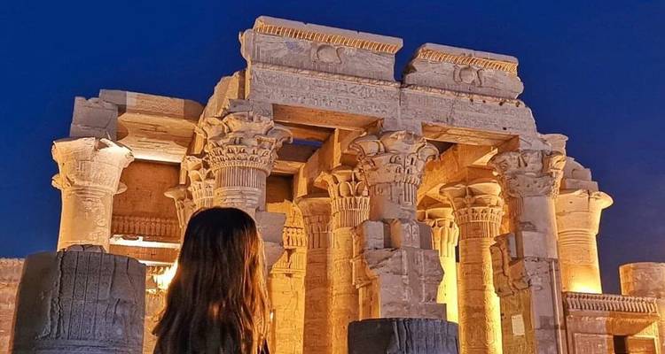 Eine Frau in der Nähe von beleuchteten altägyptischen Säulen bei Nacht.