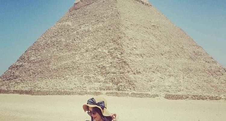 Eine Frau mit einem Hut, die bei der Großen Pyramide von Gizeh sitzt.