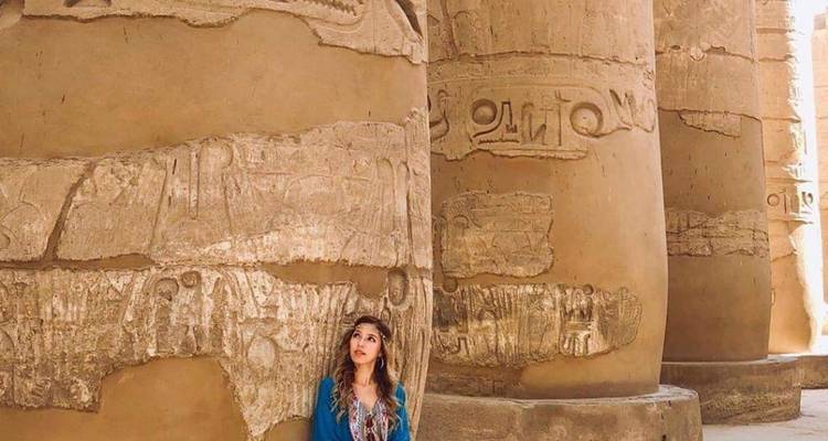 Eine Frau, die sich gegen eine altägyptische Säule mit Hieroglyphen lehnt.