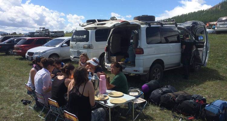 Personas teniendo un picnic junto a un vehículo.