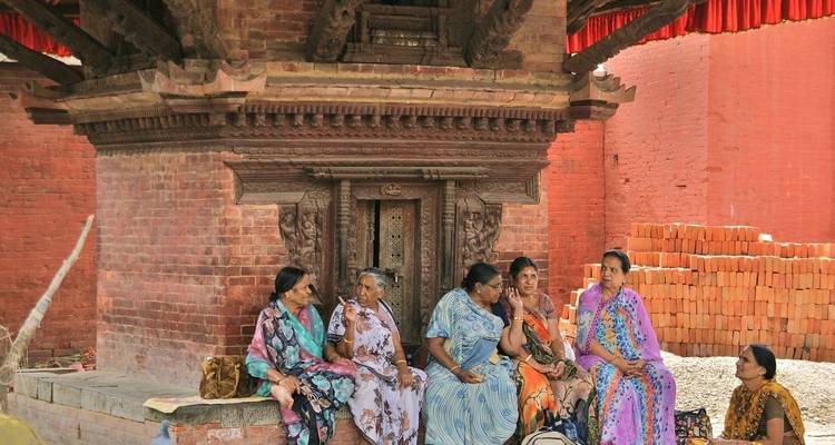 Group of elderly women sitting and talking near a traditional brick building.