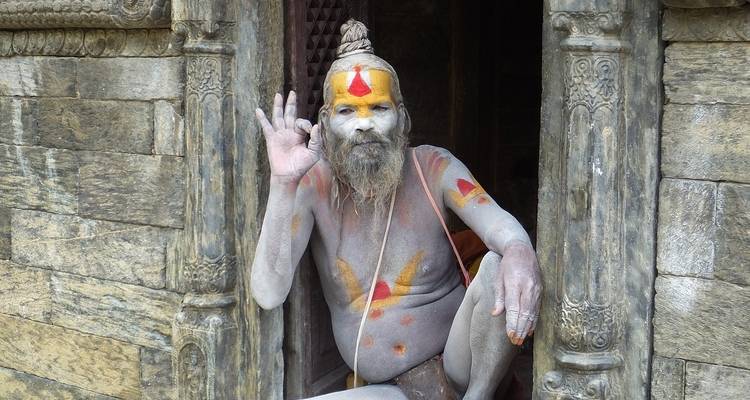 Sadhu with painted face greeting visitors in a temple entrance.