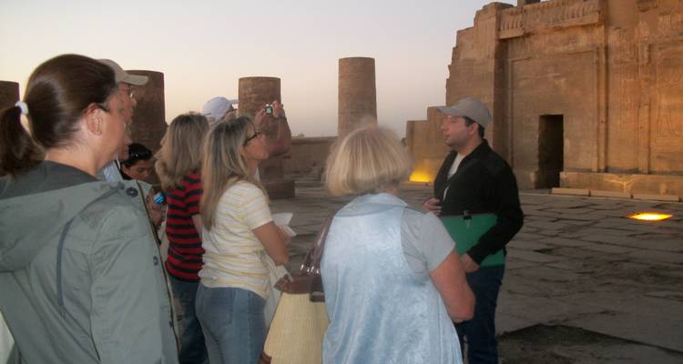 Grupo de turistas escuchando a un guía en un templo egipcio al anochecer.