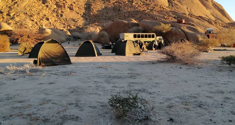 Un camping dans un cadre désertique rocheux avec un gros véhicule en arrière-plan.