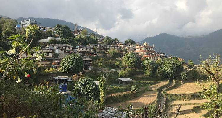 Village en terrasses à flanc de colline avec une végétation luxuriante et un ciel nuageux.