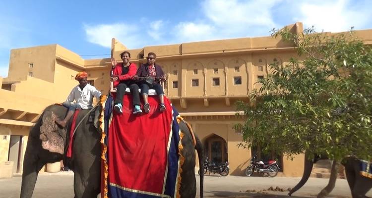 People riding an elephant in front of a historic building.