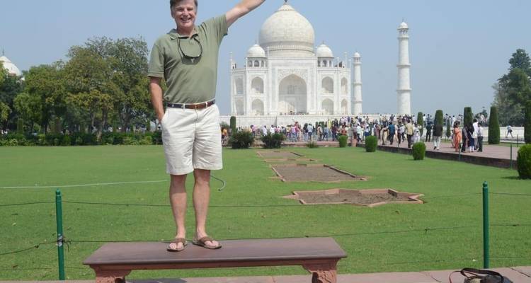 Man posing in front of the Taj Mahal, standing on a bench.