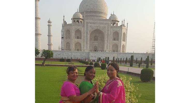 Three women in colorful saris posing in front of the Taj Mahal.