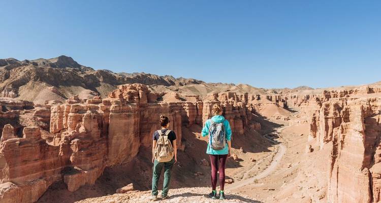 Twee wandelaars die uitkijken over een uitgestrekt canyonlandschap.