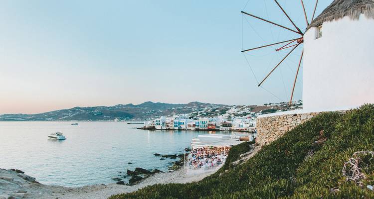 Vue d'un moulin à vent au bord de la mer avec des gens qui dînent au coucher du soleil.