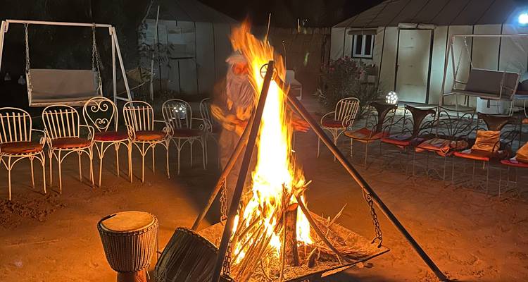 Lagerfeuerszene bei Nacht mit Zelten und Menschen, die rundherum sitzen.