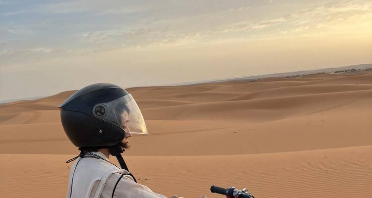 Person auf einem Motorrad mit Blick auf weite Sanddünen bei Sonnenuntergang.