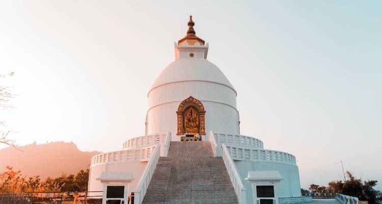 Stupa blanc avec des escaliers qui mènent vers le haut, contre un ciel serein.