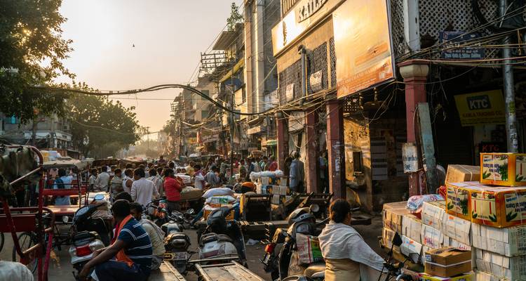 Drukke straat in het Oude Delhi vol scooters, karren en marktkraampjes in het warme middaglicht.