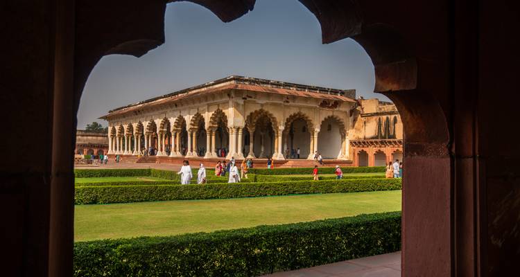 Bezoekers wandelen door de zuilen zaal voor audiënties van het Agra Fort, omlijst door een boogpoort.