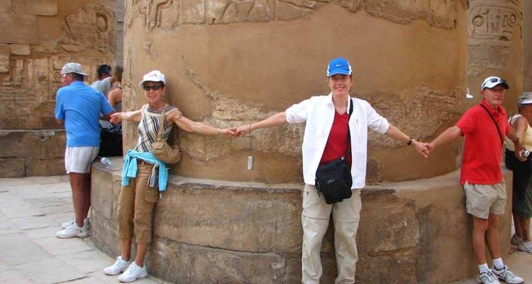 Turistas tomados de la mano alrededor de una columna antigua con grabados.