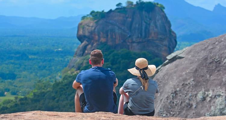 Stel zittend op een rots met uitzicht op een berg en bos.