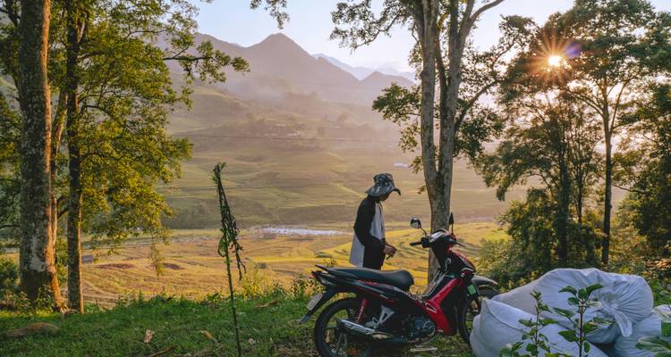 Motocycliste s'arrêtant au lever du soleil pour contempler les rizières en terrasses brumeuses près de Sapa.