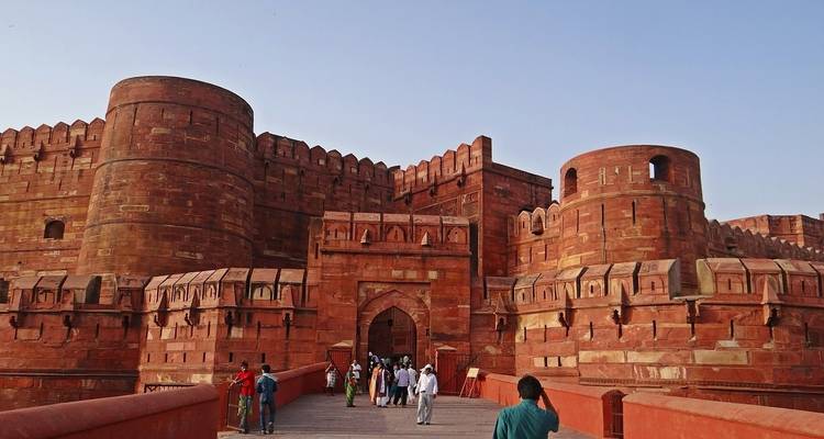 Massive red fort with tourists entering through a gate.