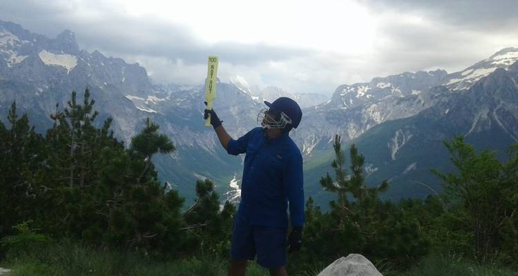 Person mit einem Cricketschläger auf einem Berggipfel.