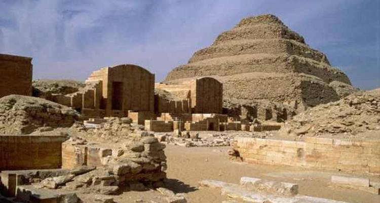 Altägyptische Stufenpyramide des Djoser erhebt sich über zerstörten Steinhöfen unter blauem Himmel
