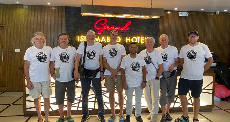 Zeven trekkers in bijpassende witte expeditie-shirts poseren in de lobby van het Grand Islamabad Hotel.
