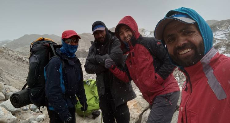 Excursionistas sonrientes se acurrucan juntos para una selfie mientras cae nieve ligera en un sendero de gran altitud.