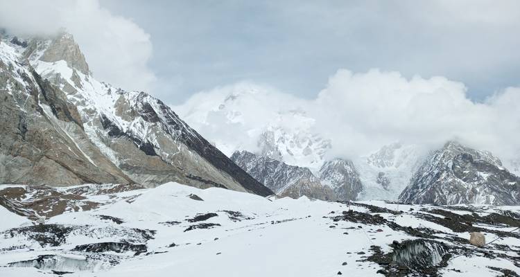 Dramáticos picos de granito cubiertos de nieve y glaciares se alzan sobre un amplio valle blanco bajo nubes dispersas.