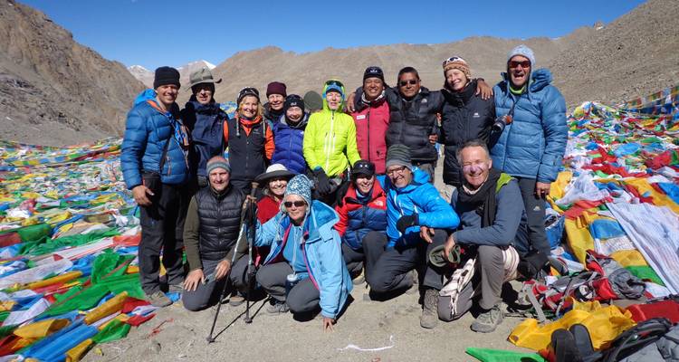 Group of tourists sitting in front of a mountain landscape with colorful flags.