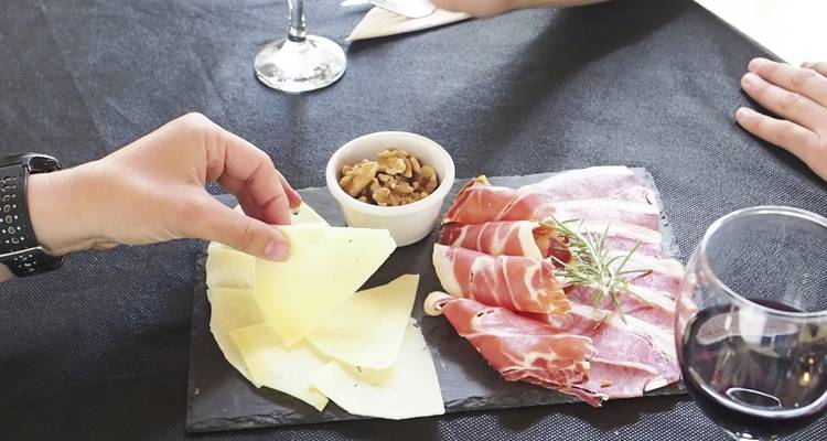 Une assiette de fromage, de charcuterie et de noix sur une table avec un verre de vin.