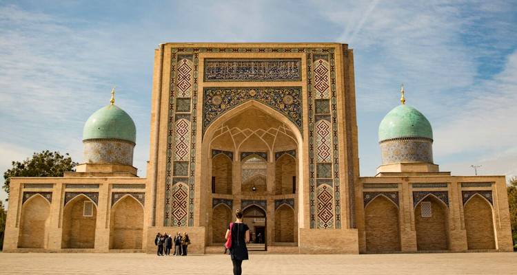 Visitor approaches a grand tiled madrasa with turquoise domes in Tashkent.