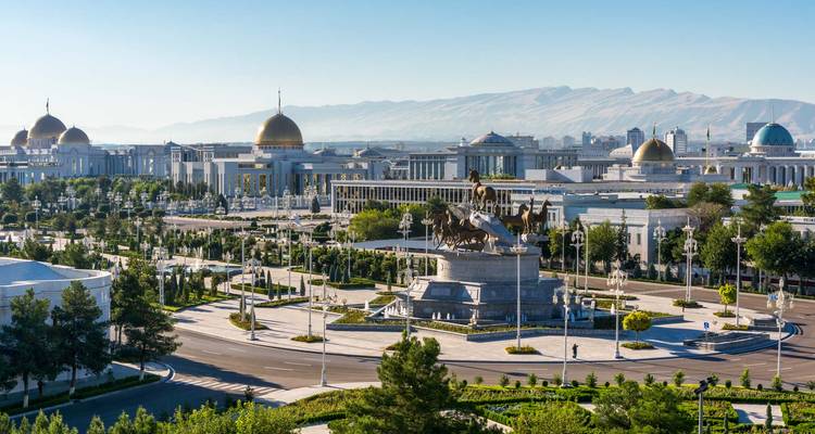 Large vue panoramique d'Achgabat présentant des bâtiments blancs majestueux, des dômes et des montagnes lointaines.