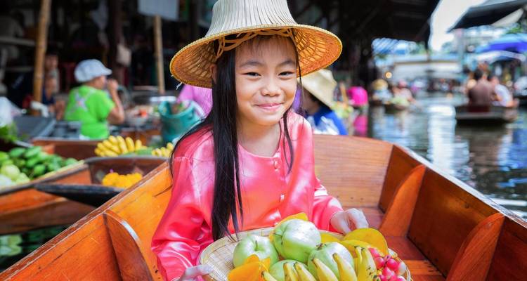 A child in a boat holding tropical fruits in a floating market.