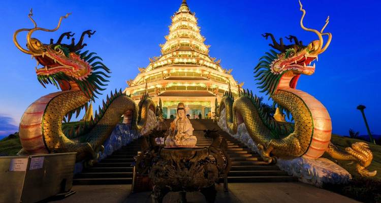 A grand temple with dragon sculptures and a lit staircase at dusk.
