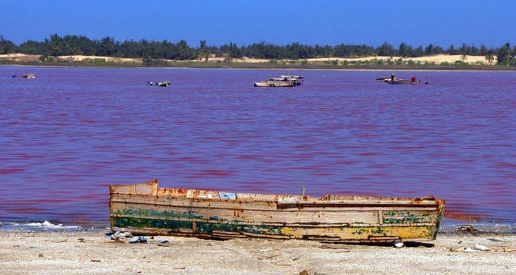 Un lac rose avec des bateaux et une rive sablonneuse avec un bateau en bois.