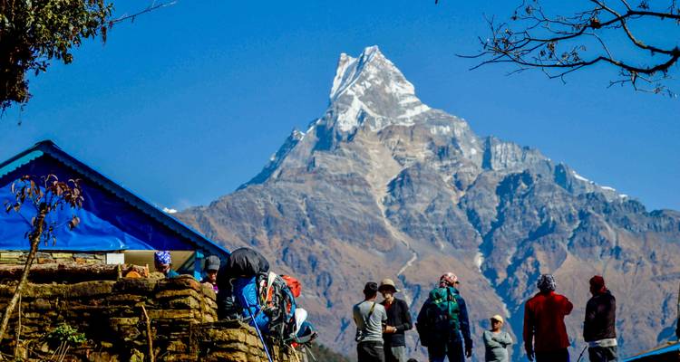Mensen die staan bij een huis met een met sneeuw bedekte berg op de achtergrond.