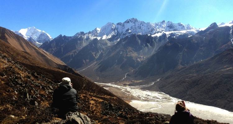 Two people sitting on rocks with a view of snowy mountains.
