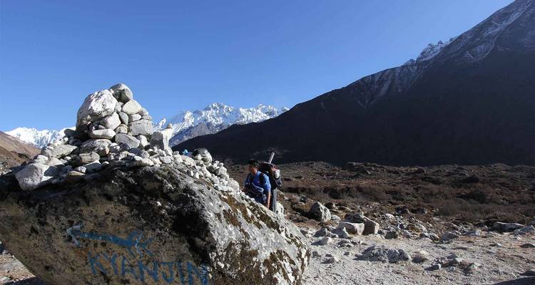 Two people walking by a rocky terrain with snowy mountains.