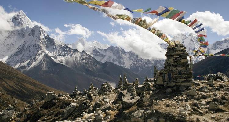 Prayer flags blowing in the wind near rocky terrain and snowy peaks.
