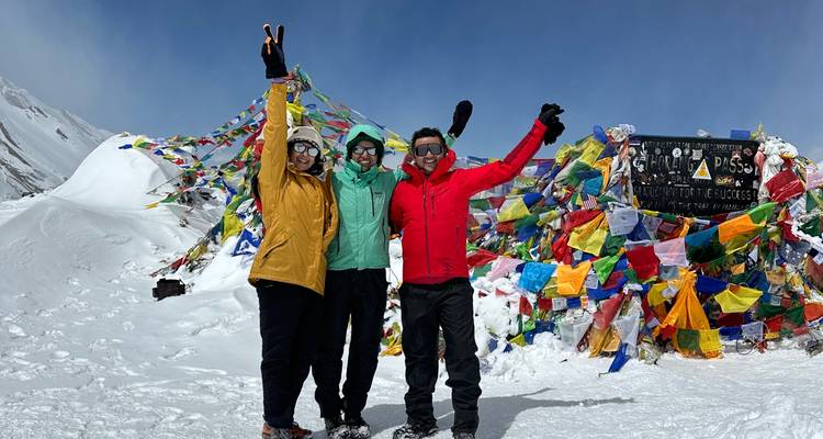Drie wandelaars die poseren met vlaggen bij de Thorong La Pass.