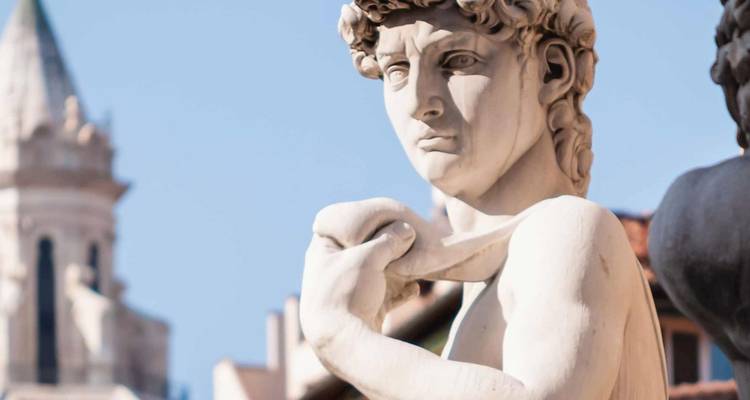 La estatua del David de Miguel Ángel mira intensamente contra un cielo florentino azul claro