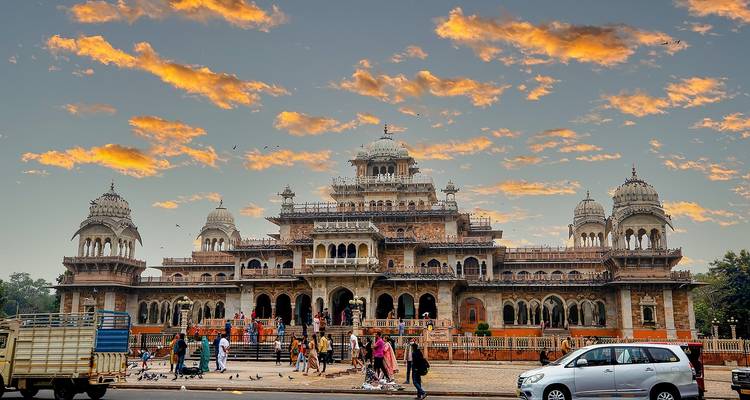 Museo Albert Hall iluminado contra un cielo de atardecer naranja vívido con visitantes reunidos al frente.