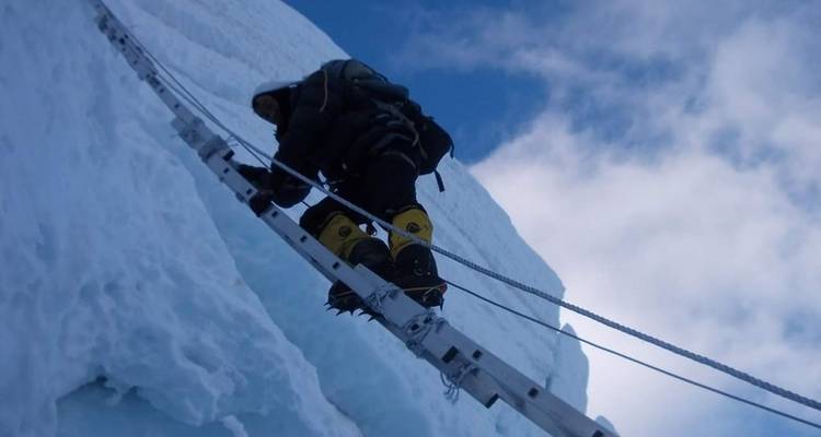 Kletterer, der einen verschneiten Hang mit Seil und Leiter erklimmt.
